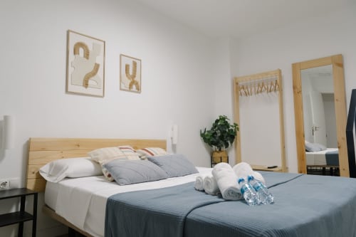 Dormitorio moderno en Stay Gest Valencia con cama de madera, ropa de cama gris, almohadas blancas, espejos y arte de pared