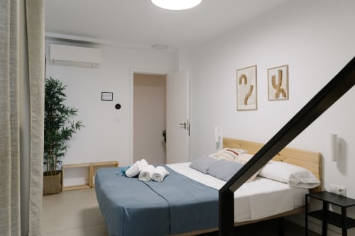 Dormitorio moderno en Stay Gest Valencia con camas de madera, ropa de cama azul y blanca, paredes blancas y decoración minimalista
