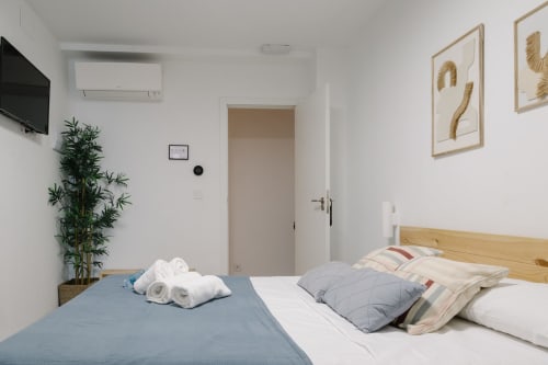 Habitación moderna en Stay Gest Valencia con cama de madera, ropa de cama azul y blanca, TV montada en pared, planta verde y cuadros decorativos