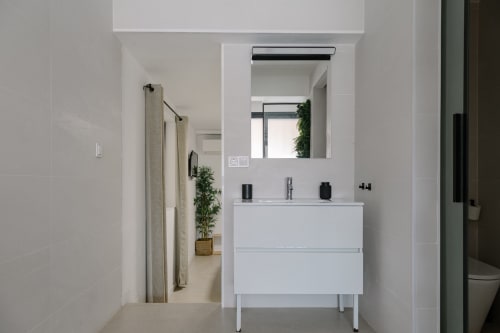 Baño moderno de color blanco en Stay Gest Valencia con lavabo flotante, espejo grande y diseño minimalista