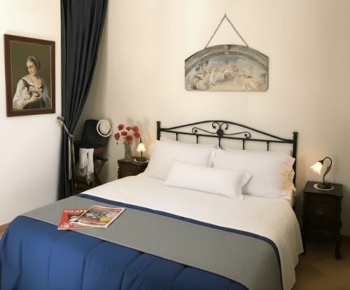 Camera doppia al Candalù Hotel con letto in ferro battuto, biancheria bianca, plaid blu, vista giardino e arredamento classico