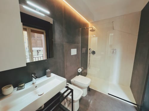 Moderno bagno dell'Hotel Candalù a Valderice con parete in piastrelle nere, lavabo bianco, WC e doccia walk-in