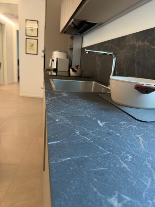 Cucina moderna con piano di lavoro in marmo nero, lavello in acciaio inossidabile e elettrodomestici bianchi nell'appartamento La Carezza di Arco