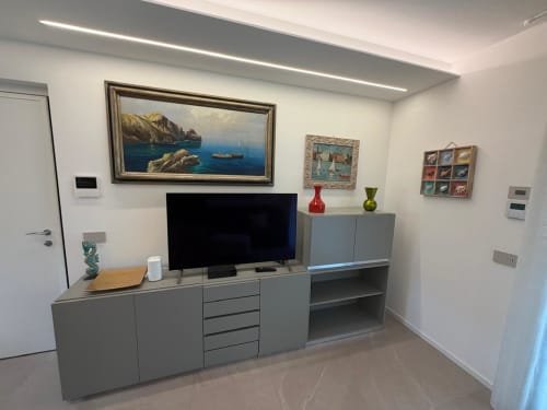 Soggiorno moderno con TV, unità di stoccaggio grigie e opere d'arte incorniciate nell'appartamento La Carezza di Arco