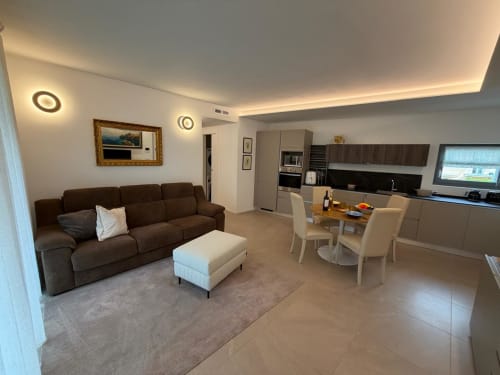 Moderno appartamento open-plan ad Arco con divano marrone, zona pranzo e cucina attrezzata con vista sul giardino