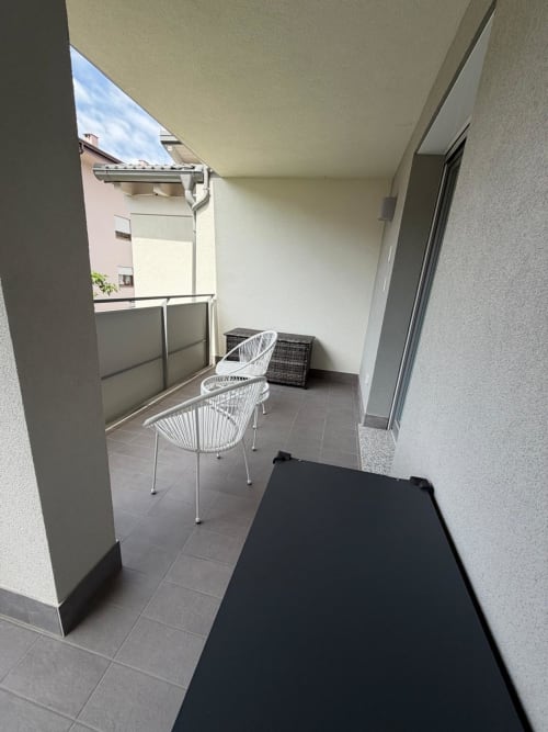 Terrazza coperta dell'appartamento La Carezza di Arco con sedie bianche, pavimento scuro e vista sugli edifici circostanti