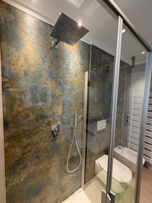 Bagno moderno con rivestimento in piastrelle grigie texture, soffione a cascata e zona doccia in vetro a La Carezza di Arco