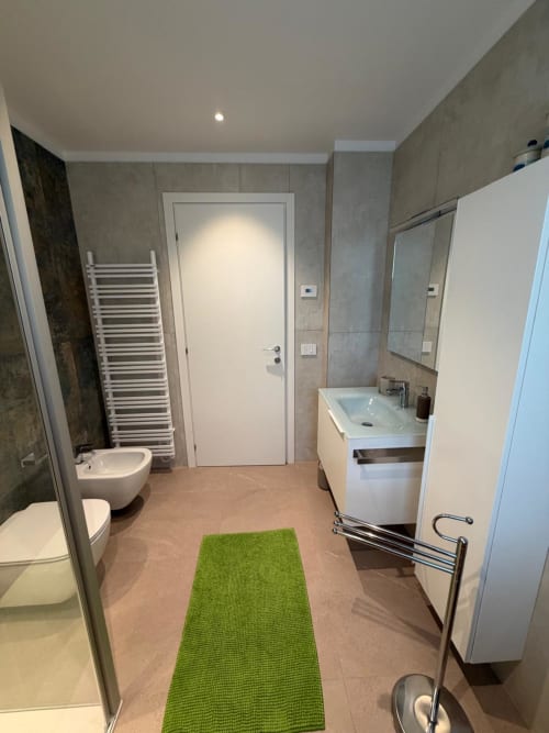 Bagno moderno dell'appartamento La Carezza di Arco con lavabo, wc, bidet, scaldasalviette e tappetino verde
