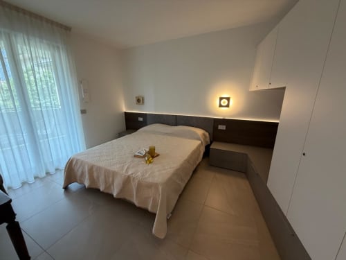 Camera da letto moderna nell'appartamento La Carezza di Arco con letto queen-size, testata scura, illuminazione d'ambiente e vista sul giardino