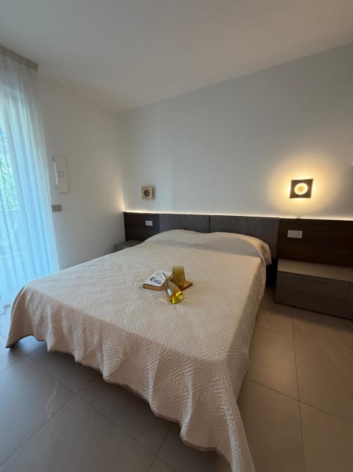 Camera da letto moderna con letto queen, testata scura, illuminazione ambientale e vista sul giardino presso Holiday Home Garda Trentino, Arco