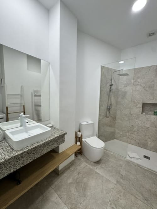 Baño de apartamento moderno en Madrid con doble lavamano, ducha de lluvia y acabados en azulejos grises en Artbel Rentals