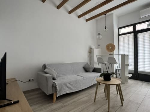 Sala de estar moderna de apartamento madrileño con sofá gris, vigas de madera, lámparas colgantes y acceso a balcón en Artbel Rentals