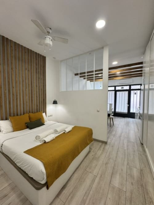 Dormitorio moderno en apartamento Artbel Rentals Madrid con cama blanca, detalles mostaza, suelo tipo madera y tabique de cristal