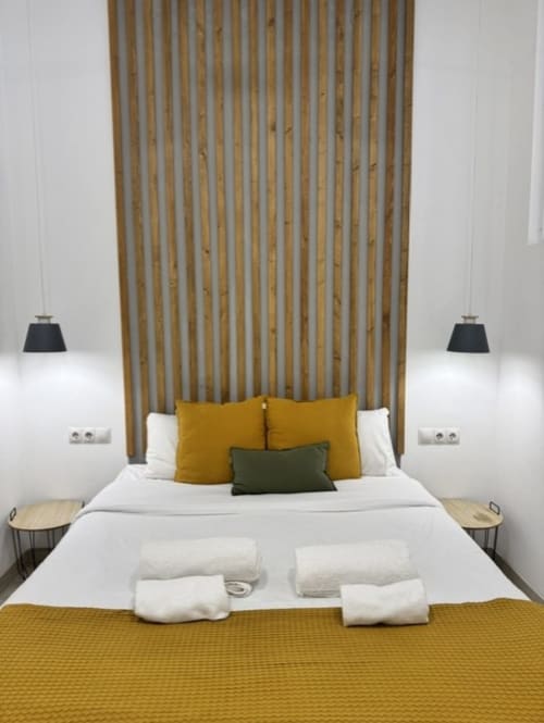 Dormitorio moderno en Artbel Rentals Madrid con cama blanca, almohadas mostaza y oliva, cabecero de listones de madera, luces colgantes