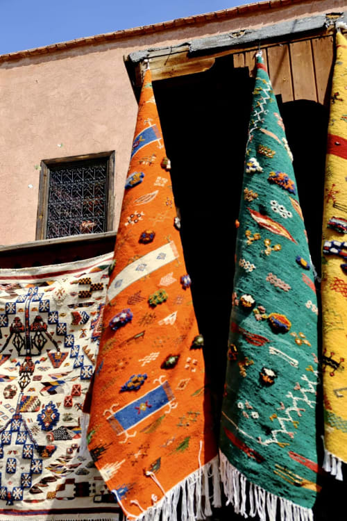 Colorful traditional carpets hanging outside Riad 191 in Marrakech with ornate window and terracotta walls