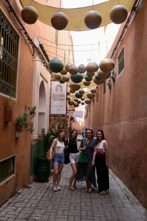 Four guests in a colorful narrow alley at Riad 191 Marrakech, decorated with hanging bronze spheres