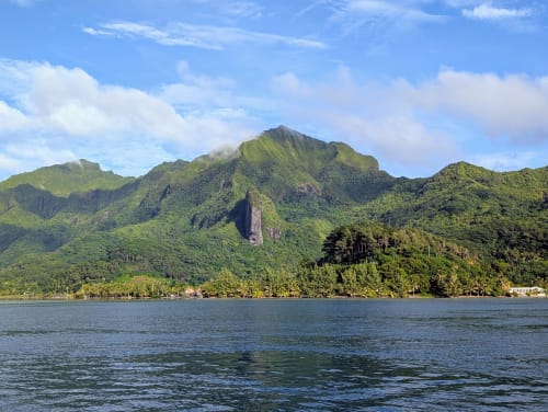 Des montagnes verdoyantes s'élèvent derrière des eaux cristallines à Raiatea, Polynésie française, où se trouvent les bungalows balnéaires Fare Tihi Moana