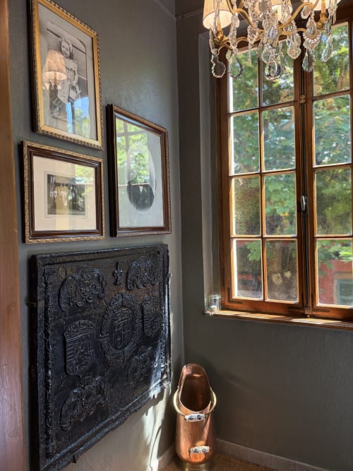 Détail élégant à l'Hôtel l'Ange : panneau noir en relief orné, œuvre encadrée, lustre en cristal et hautes fenêtres
