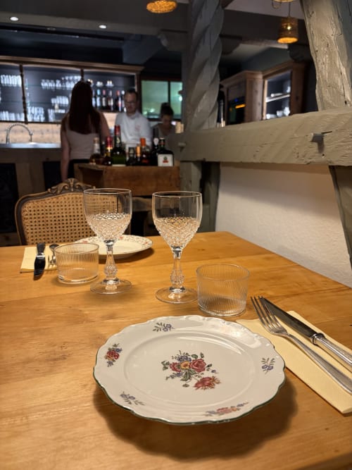 Table élégamment dressée au restaurant l'Ange à Niedermorschwihr avec assiette en porcelaine fleurie et verres en cristal