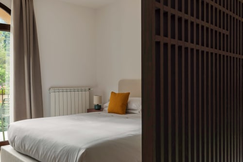 Camera moderna a Dimora Silva Nature Suites con letto bianco, cuscino arancione, divisorio in legno scuro, radiatore e vista sulle montagne
