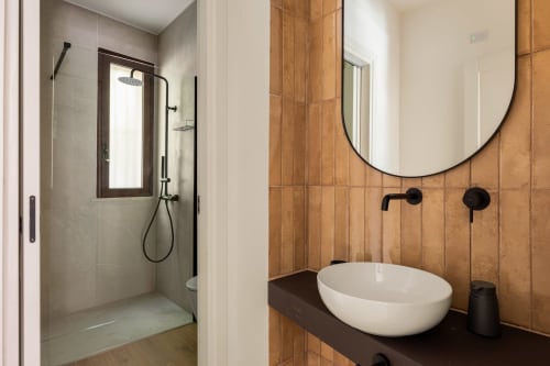Bagno moderno in Dimora Silva 3 con lavabo in marmo bianco, mattonelle in terracotta, specchio rotondo e doccia a pioggia