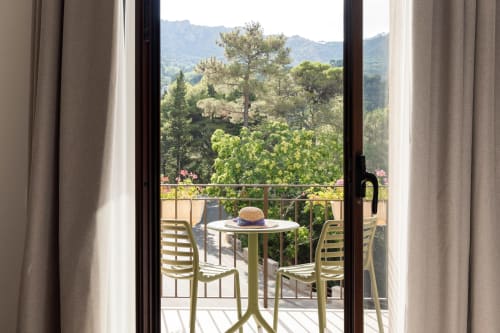 Vista dal balcone della Dimora Silva Nature Suites con paesaggio montano, colline verdeggianti, cappello di paglia sul tavolo e patio moderno