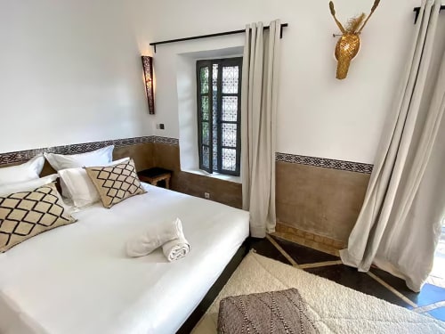 Chambre élégante du Riad 191 à Marrakech avec literie blanche, coussins géométriques, décor tête d'antilope dorée et style traditionnel