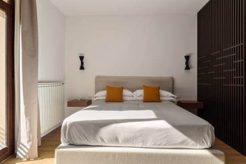 Camera moderna presso Dimora Silva Nature Suites con letto beige, cuscini arancioni, pannelli scuri e vista montagna