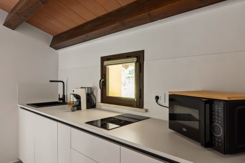 Moderna angolo cottura presso Dimora Silva Nature Suites con mobili bianchi, microonde, piano cottura, travi in legno e finestra