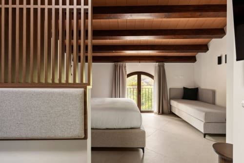 Camera moderna a Dimora Silva Nature Suites con travi in legno a vista, letto, divano e vista montagna attraverso la porta ad arco