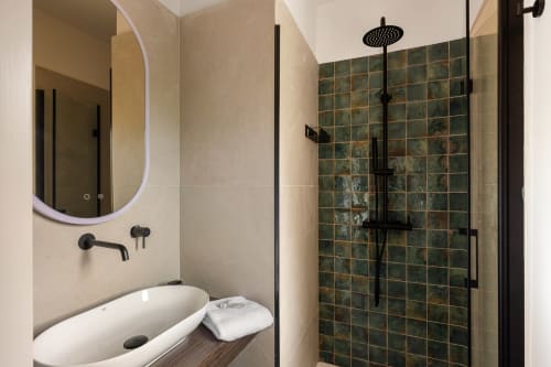 Bagno moderno presso Dimora Silva Nature Suites con specchio rotondo, rubinetteria nera, lavabo da appoggio e doccia rivestita in piastrelle verdi