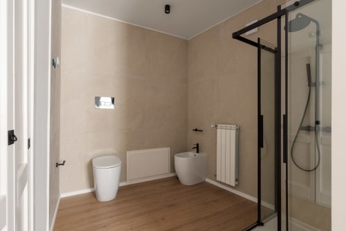Bagno moderno a Dimora Silva 8 con wc, lavabo, radiatore bianco e doccia con box in vetro nero e soffione pioggia