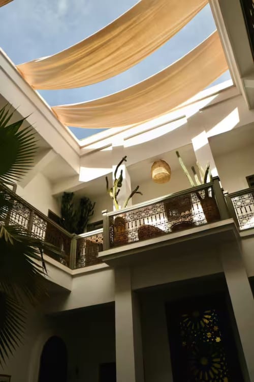 Cour du Riad 191 à Marrakech avec murs blancs, balustrades décoratives, voiles d'ombrage beiges et puits de lumière ouvert sur le ciel bleu