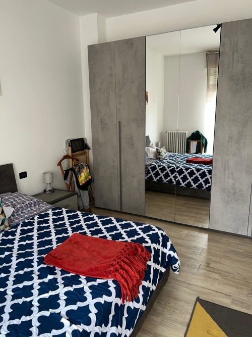 Camera moderna negli Appartamenti MiSaNi di Novara con armadio a specchio, biancheria da letto blu a motivi e pavimenti in legno