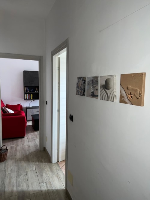 Corridoio dell'appartamento MiSaNi Orchidea a Novara, con pareti bianche, pavimento in legno, quattro opere d'arte incorniciate e porta aperta verso