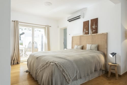 Bright modern bedroom with rattan headboard, pool view doors, AC unit, and wooden floors at RB Algarve villa in Boliqueime,