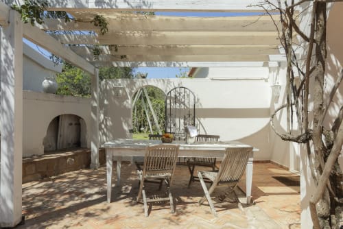 Shaded patio at RB Algarve villa in Boliqueime with dining table, wooden chairs, pergola, fireplace, and climbing vines
