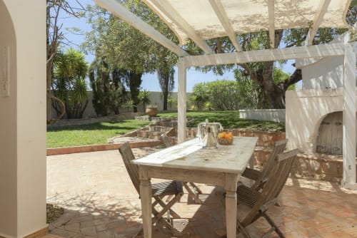 Shaded patio dining area with wooden table and chairs overlooking manicured garden at RB Algarve villa in Boliqueime,