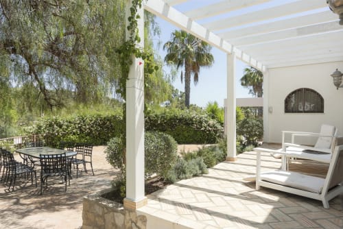 Spacious patio at RB Algarve villa with white pergola, lounge chairs, dining area, lush greenery and palm trees in