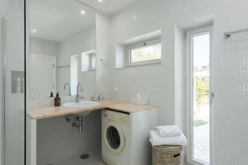 Modern bathroom at RB Algarve villa with white tile walls, wooden countertop, sink, washing machine, and glass shower