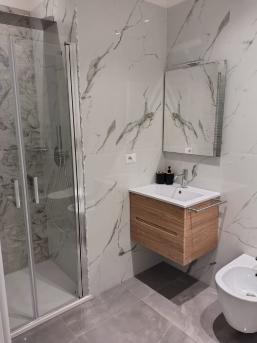 Moderno bagno della BellDuomo Suite Messina con pareti in marmo, mobile in legno, doccia e specchio