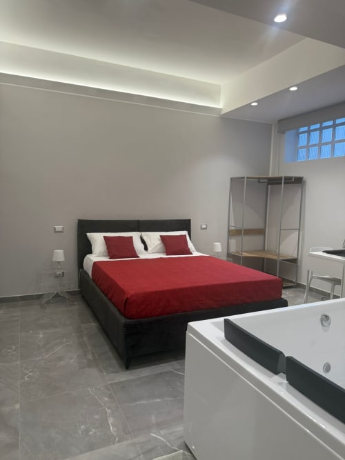 Camera moderna della BellDuomo Suite Messina con letto nero, biancheria rossa, vasca bianca e pavimento in marmo