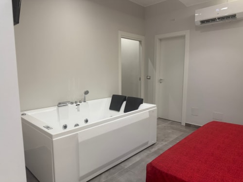 Bagno moderno con vasca idromassaggio, cuscini neri, porte bianche e letto rosso della suite BellDuomo Messina