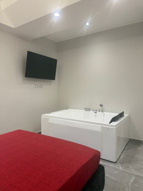 Camera moderna della BellDuomo Suite Messina con letto rosso, TV a parete e lussuosa vasca jacuzzi in bagno ensuite