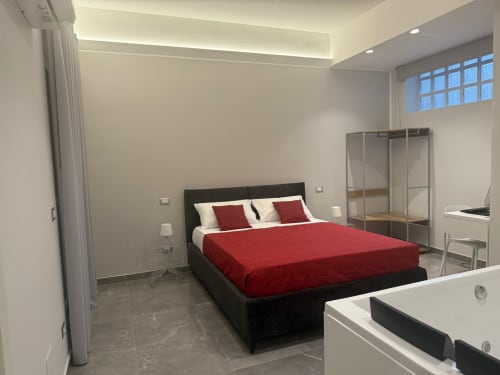 Camera moderna a BellDuomo Suite Messina con biancheria rossa, letto con struttura nera, armadio specchiato e vista sulla città