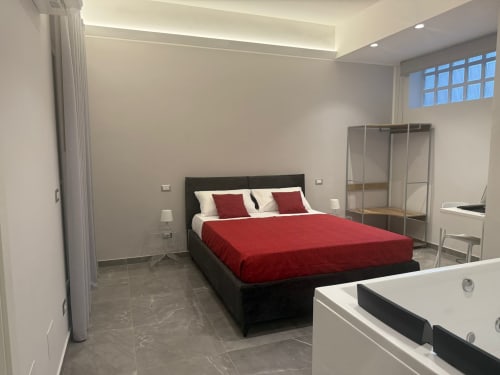 Camera moderna di BellDuomo Suite Messina con letto nero, biancheria rossa, vasca idromassaggio e vista sulla città