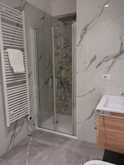Bagno moderno con pareti in marmo, cabina doccia in vetro, scaldasalviette e mobile lavabo in legno presso BellDuomo Suite Messina