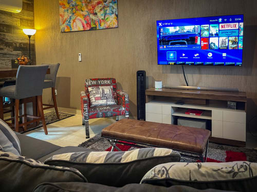 Sala moderna con televisor 4K, servicios de streaming, otomano de cuero, sofá cama y silla temática de Nueva York en Santiago