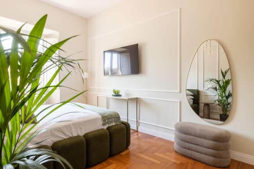 Camera da letto in moderno monolocale romano con pavimento in legno, TV, specchio curvo, piante verdi e arredi contemporanei