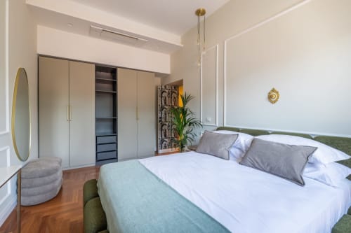 Camera da letto moderna a Roma con letto matrimoniale, dettagli verdi, armadio, specchio rotondo e pavimento in legno